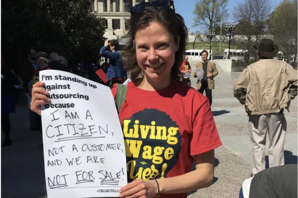 A photo of Sarah Vandergrift Eldridge holding a sign that reads "I'm standing up against outsourcing because I am a citizen, not a customer and we are not for sale!"